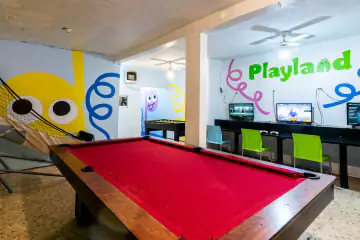 Mesa de billar de paño rojo de Playland, con las consolas de videojuegos al fondo