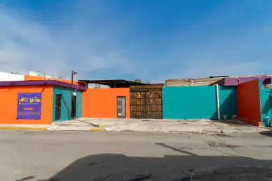 Fachada de Playland desde la calle: muros naranja y turquesa y el portón de madera de la entrada