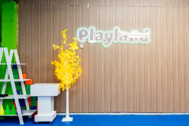 El letrero luminoso de Playland sobre el muro de madera, con un árbol de luces amarillo al lado