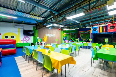 El salón de Playland montado con mesas de mantel amarillo, verde y azul bajo la nave techada